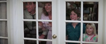 Movie still from “Poltergeist II: The Other Side” (1986), directed by Brian Gibson – A woman and two children looking out a window; Medium shot, Low angle