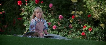 Movie still from “Poltergeist II: The Other Side” (1986), directed by Brian Gibson – A little girl sitting in the grass near some flowers; Medium shot, High angle