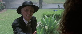 Movie still from “Poltergeist II: The Other Side” (1986), directed by Brian Gibson – An older woman wearing a black hat holding a potted plant; Medium shot, Over the shoulder angle