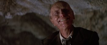 Movie still from “Poltergeist II: The Other Side” (1986), directed by Brian Gibson – An old man with a shaved head is smiling for the camera; Close Up shot, Low angle