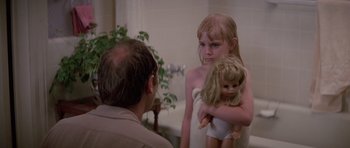 Movie still from “Poltergeist II: The Other Side” (1986), directed by Brian Gibson – A little girl holding a doll in her arms while a man looks on; Close Up shot, Over the shoulder angle