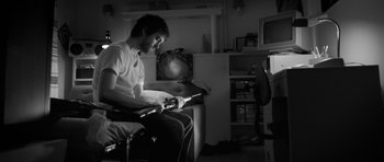Movie still from “Polytechnique” (2009), directed by Denis Villeneuve – A man sitting in front of an electric guitar in a living room; Medium shot, High angle