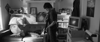 Movie still from “Polytechnique” (2009), directed by Denis Villeneuve – A young man holding a guitar in a living room; Medium shot, Over the shoulder angle