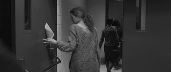 Movie still from “Polytechnique” (2009), directed by Denis Villeneuve – A woman wearing a sweater walking down a hall way; Medium shot, Over the shoulder angle
