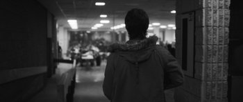 Movie still from “Polytechnique” (2009), directed by Denis Villeneuve – A person standing in front of a group of tables; Medium shot, Over the shoulder angle