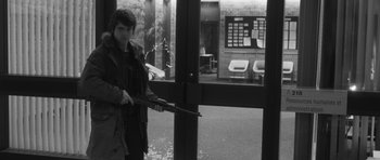 Movie still from “Polytechnique” (2009), directed by Denis Villeneuve – A person holding a gun in front of a window; Medium shot, Over the shoulder angle