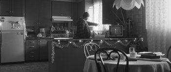 Movie still from “Polytechnique” (2009), directed by Denis Villeneuve – A person standing in a kitchen near a table and chair; Medium shot, Low angle