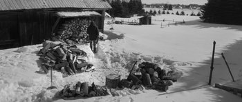 Movie still from “Polytechnique” (2009), directed by Denis Villeneuve – A person standing in the snow next to a pile of wood; Wide shot, High angle