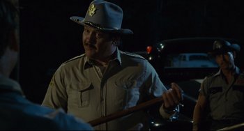 Movie still from “Porky's” (1981), directed by Bob Clark – A man wearing a hat and holding a wooden stick; Medium shot, Over the shoulder angle