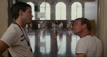 Movie still from “Porky's” (1981), directed by Bob Clark – Two men are talking in a gym with people in the background; Medium shot, Over the shoulder angle