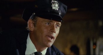 Movie still from “Porky's” (1981), directed by Bob Clark – A police officer in uniform is looking at the camera; Close Up shot, Over the shoulder angle
