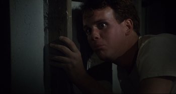 Movie still from “Porky's” (1981), directed by Bob Clark – A man leaning against a wooden post in a dark room; Close Up shot, Low angle