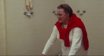 Movie still from “Porky's” (1981), directed by Bob Clark – A woman in a white shirt and a red scarf is standing in a bathroom; Medium shot, Over the shoulder angle