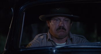 Movie still from “Porky's” (1981), directed by Bob Clark – A police officer sitting in a car at night; Close Up shot, Low angle