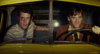 Movie still from “Porky's” (1981), directed by Bob Clark – Two young men in a yellow car looking out of the window; Medium shot, High angle