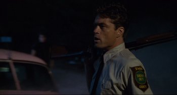 Movie still from “Porky's” (1981), directed by Bob Clark – A man in a police uniform holding a gun; Medium shot, Over the shoulder angle