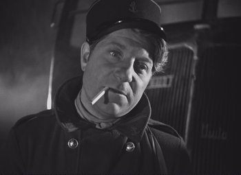 Movie still from “Port of Shadows” (1938), directed by Marcel Carné – A man wearing a hat and smoking a cigarette; Close Up shot, Low angle