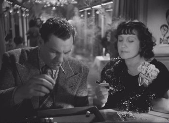 Movie still from “Port of Shadows” (1938), directed by Marcel Carné – A man and a woman sitting at a table smoking cigarettes; Medium shot, High angle