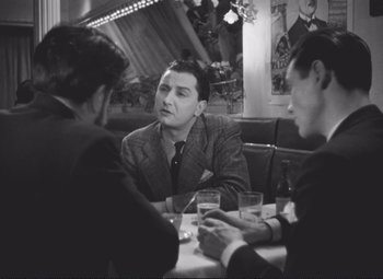 Movie still from “Port of Shadows” (1938), directed by Marcel Carné – A group of men sitting at a table with drinks; Medium shot, Over the shoulder angle
