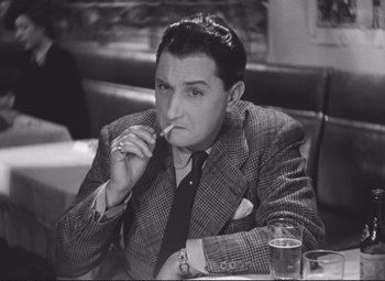 Movie still from “Port of Shadows” (1938), directed by Marcel Carné – A black and white photo of a man smoking a cigarette; Close Up shot, High angle