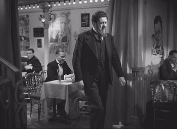 Movie still from “Port of Shadows” (1938), directed by Marcel Carné – A black and white photo of a man walking in a restaurant; Wide shot, Low angle
