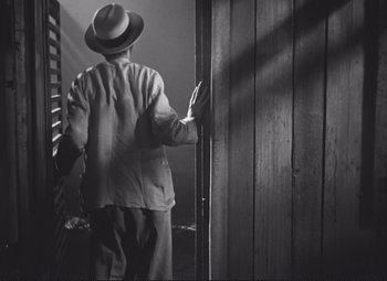Movie still from “Port of Shadows” (1938), directed by Marcel Carné – A black and white photo of a man in a hat; Medium shot, Over the shoulder angle