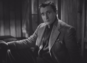 Movie still from “Port of Shadows” (1938), directed by Marcel Carné – A man sitting in a chair wearing a suit and tie; Close Up shot, Low angle