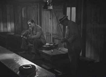 Movie still from “Port of Shadows” (1938), directed by Marcel Carné – Two men sitting on a bench in a room; Wide shot, High angle