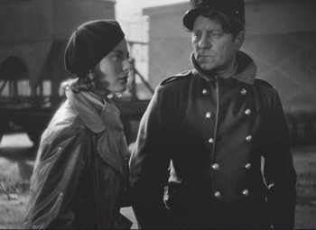 Movie still from “Port of Shadows” (1938), directed by Marcel Carné – An old photo of a man and a woman standing next to each other; Medium shot, Over the shoulder angle