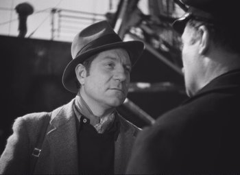 Movie still from “Port of Shadows” (1938), directed by Marcel Carné – A black and white photo of a man wearing a hat; Close Up shot, Over the shoulder angle