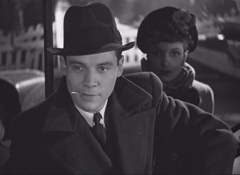 Movie still from “Port of Shadows” (1938), directed by Marcel Carné – A man in a hat smoking a cigarette next to a woman in a hat; Close Up shot, Low angle