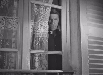 Movie still from “Port of Shadows” (1938), directed by Marcel Carné – A black and white photo of a man looking out of a window; Medium shot, Low angle