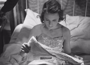 Movie still from “Port of Shadows” (1938), directed by Marcel Carné – A young woman reading a newspaper in bed; Medium shot, High angle