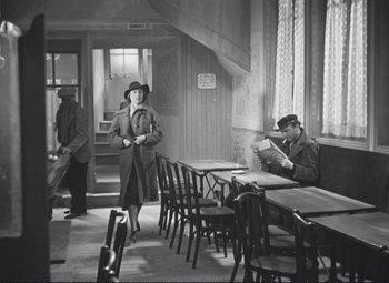 Movie still from “Port of Shadows” (1938), directed by Marcel Carné – A woman and a man are standing in a restaurant; Wide shot, High angle