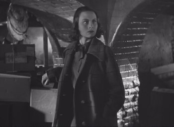 Movie still from “Port of Shadows” (1938), directed by Marcel Carné – A black and white photo of a woman in a trench coat; Medium shot, Low angle