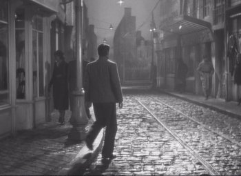Movie still from “Port of Shadows” (1938), directed by Marcel Carné – A man walking down a street at night; Wide shot, High angle