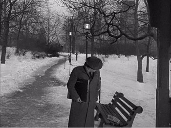 Movie still from “Portrait of Jennie” (1948), directed by William Dieterle – A man standing next to a bench in the snow; Wide shot, High angle