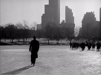 A man walking across a frozen pond in a city