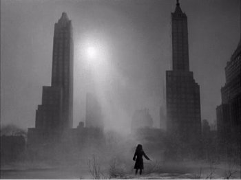 Movie still from “Portrait of Jennie” (1948), directed by William Dieterle – A person walking in the fog in front of some tall buildings; Extreme Wide shot, Low angle