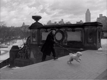 Movie still from “Portrait of Jennie” (1948), directed by William Dieterle – A man walking a dog on a leash on a bridge; Wide shot, High angle