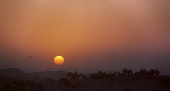 Movie still from “Powaqqatsi” (1988), directed by Godfrey Reggio – A group of people standing on top of a dirt field; Extreme Wide shot, Low angle