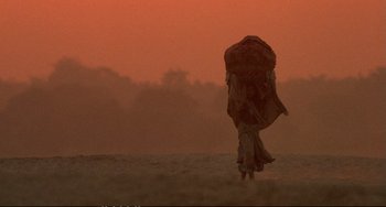 Movie still from “Powaqqatsi” (1988), directed by Godfrey Reggio – A person walking in a field with an umbrella in the distance; Extreme Wide shot, Low angle