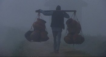 Movie still from “Powaqqatsi” (1988), directed by Godfrey Reggio – A man carrying bags in the middle of a foggy field; Wide shot, Low angle