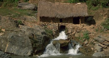 Movie still from “Powaqqatsi” (1988), directed by Godfrey Reggio – A house that is next to a waterfall; Extreme Wide shot, High angle