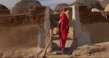 Movie still from “Powaqqatsi” (1988), directed by Godfrey Reggio – A woman in a red sari walking through a doorway; Wide shot, High angle