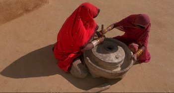 Movie still from “Powaqqatsi” (1988), directed by Godfrey Reggio – A woman in a red dress is making pottery on a wheel; Medium shot, Overhead angle