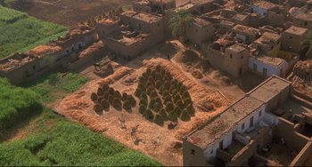 Movie still from “Powaqqatsi” (1988), directed by Godfrey Reggio – An aerial view of a village with a lot of hay; Extreme Wide shot, Overhead angle