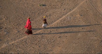 Movie still from “Powaqqatsi” (1988), directed by Godfrey Reggio – Two women in traditional dress walking on a dirt road; Extreme Wide shot, High angle