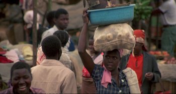 Movie still from “Powaqqatsi” (1988), directed by Godfrey Reggio – A woman carrying a bag on top of her head; Medium shot, Over the shoulder angle