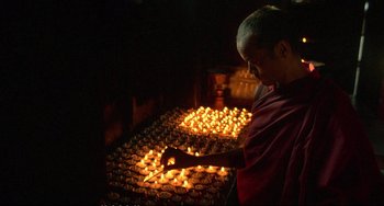 Movie still from “Powaqqatsi” (1988), directed by Godfrey Reggio – A man lighting candles in a dark room; Medium shot, High angle